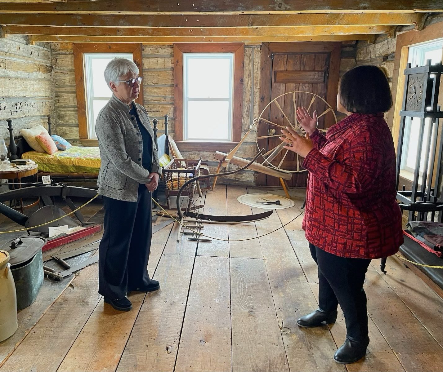 Mme Dumont, debout dans la cabane en rondins du Amherstburg Freedom Museum, écoute Mme Irene Moore Davis, conservatrice adjointe par intérim, lui expliquer l’utilisation de la pièce.