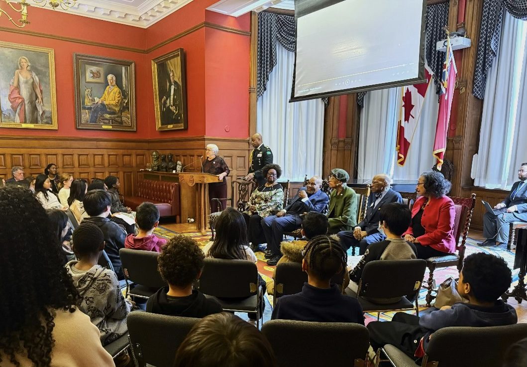 Un groupe d’élèves écoutent les propos de Mme Dumont, tandis qu’elle se tient debout à un lutrin, à côté (de gauche à droite) de Jean Augustine, de Denham Jolly, de Zanana Akande, d’Arthur Downes et de Rosemary Sadlier.